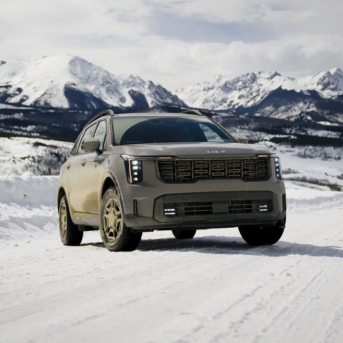 A 2025 Kia Sorento SUV driving through snowy mountain terrain with a scenic backdrop.