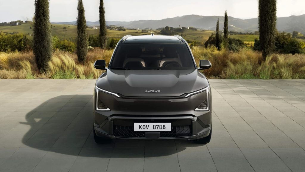 Picture of the front of a 2027 Kia EV5 in a paved lot in front of a field.