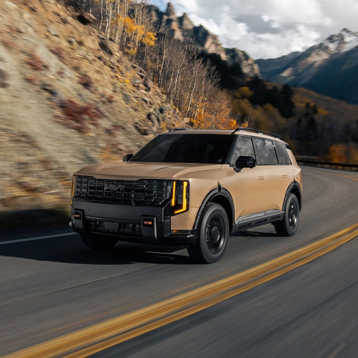 Picture of a sand coloured 2027 Kia Telluride driving up the side of a mountain.
